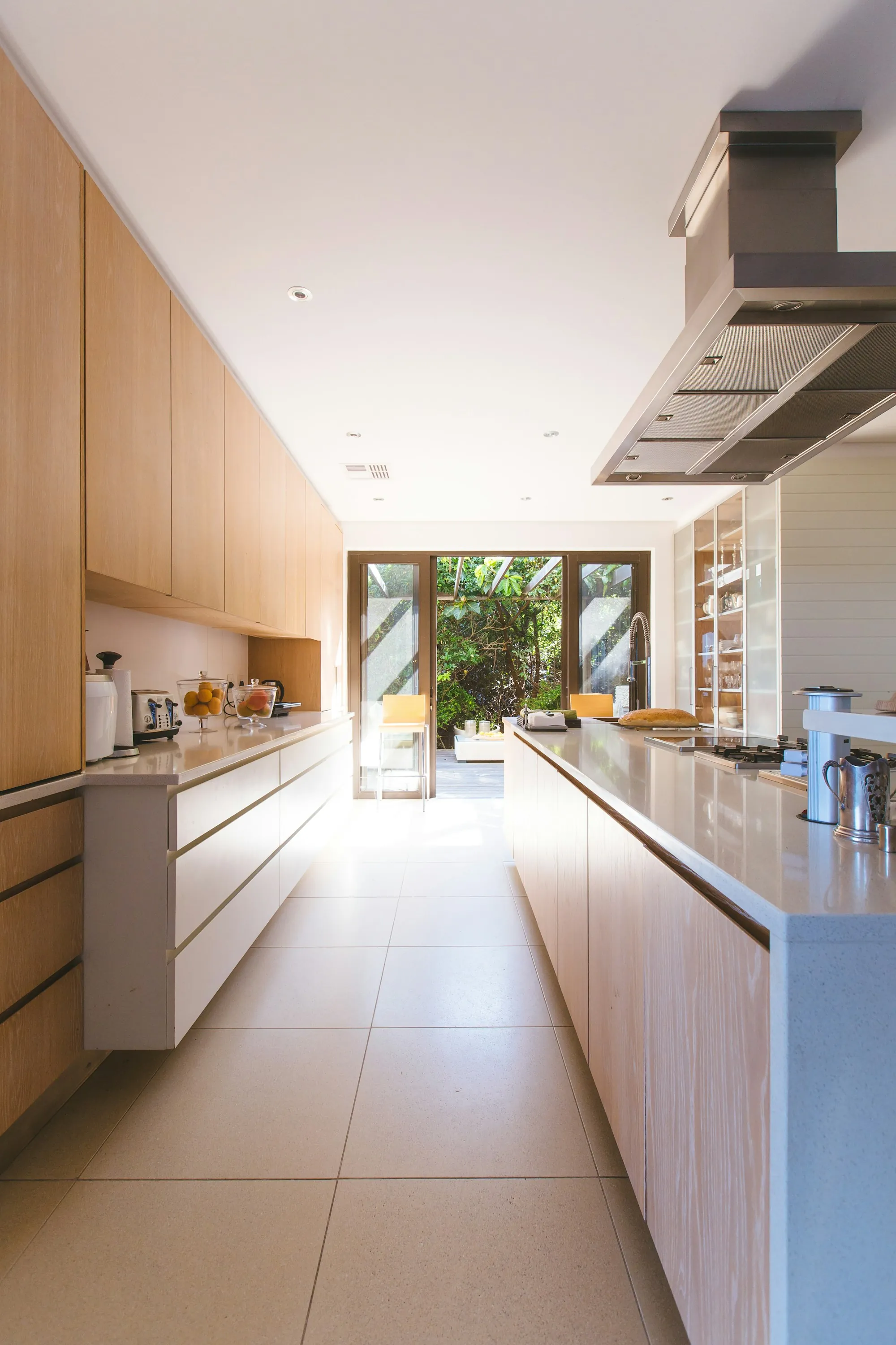 Galley kitchen with wood cabinets, a long counter and glass doors open to a garden