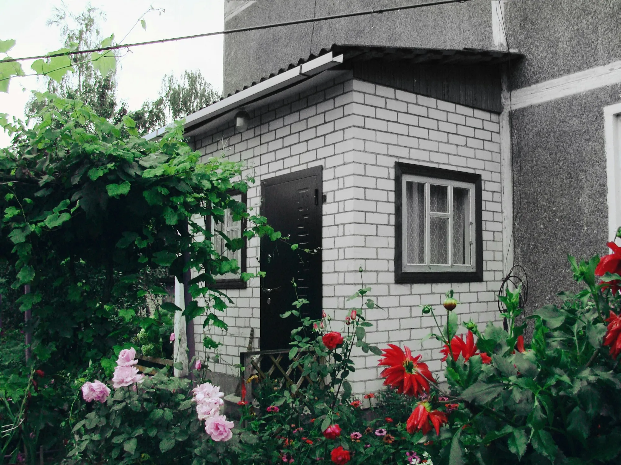 Small white-brick outbuilding with a dark door and a flowering garden in front