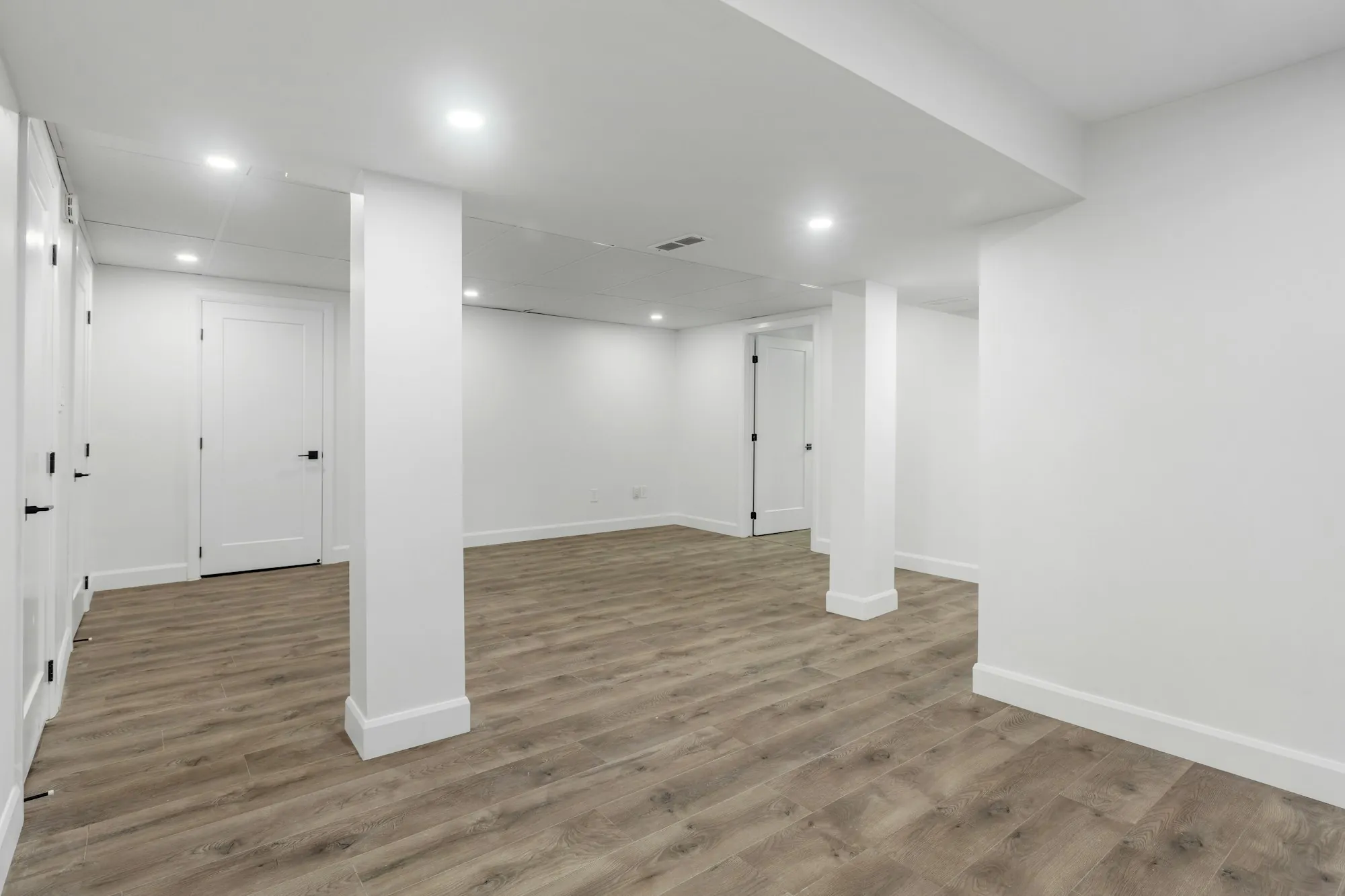 Finished basement with white columns, recessed lights and wood-look flooring