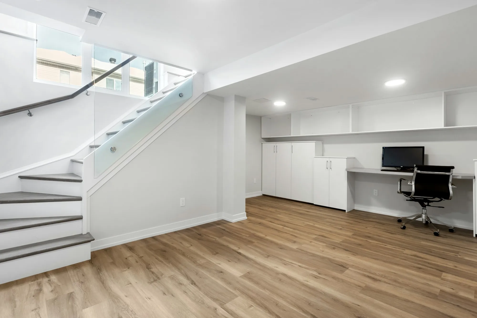 Finished basement with a glass-rail staircase, built-in storage and a desk nook