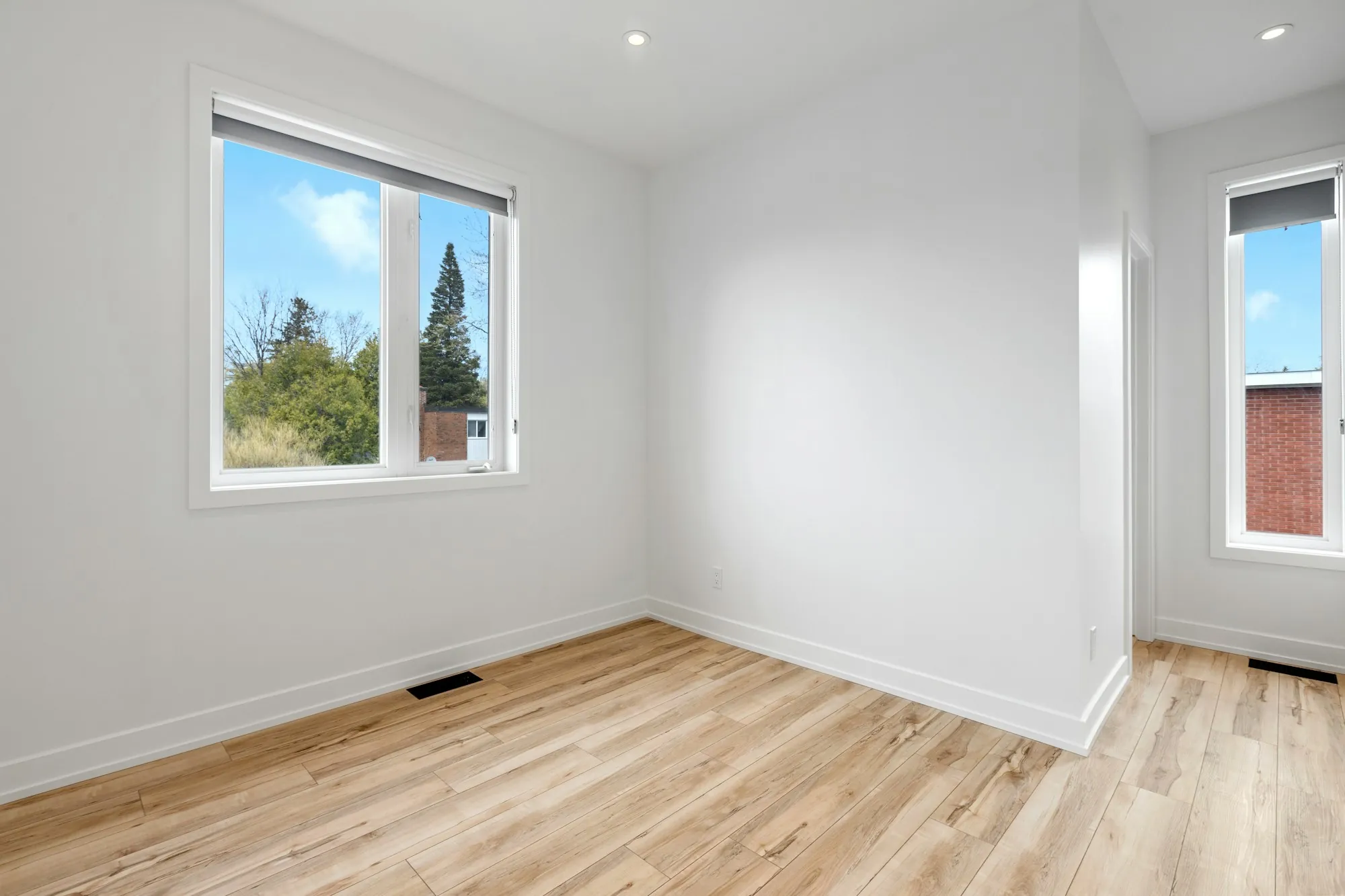 Freshly painted white room with new light wood floors and large windows