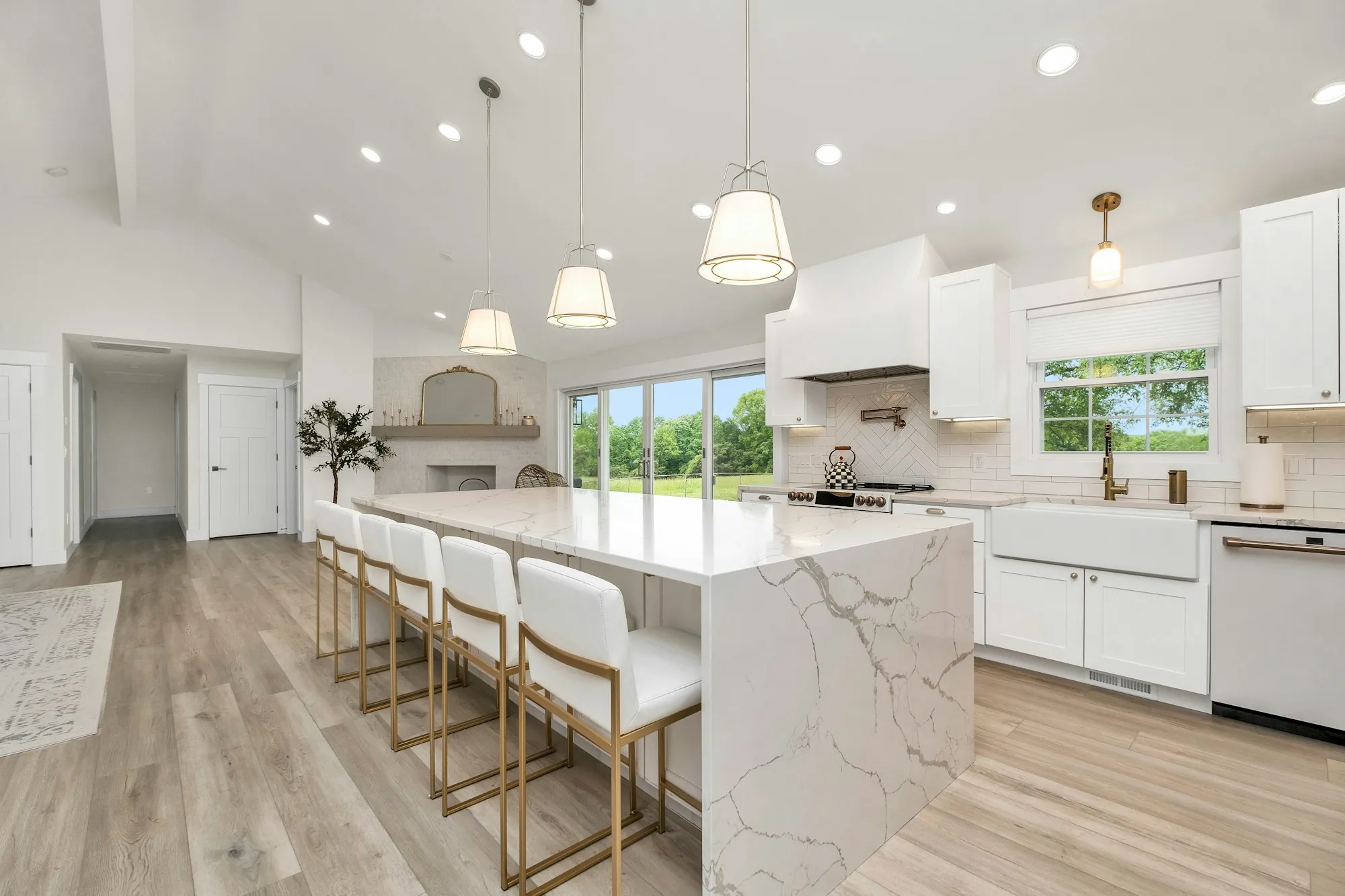 Open kitchen with a waterfall marble island, white stools and pendant lights