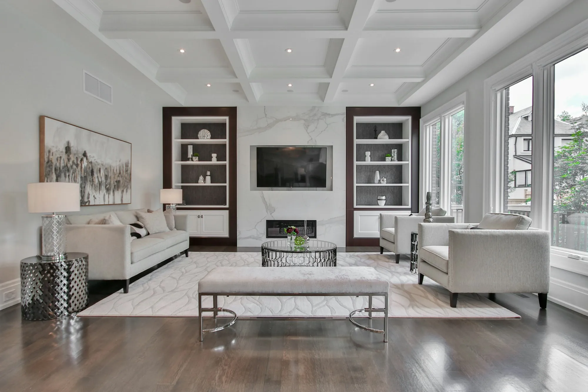 Renovated living room with a coffered ceiling, built-in shelves and a marble fireplace wall