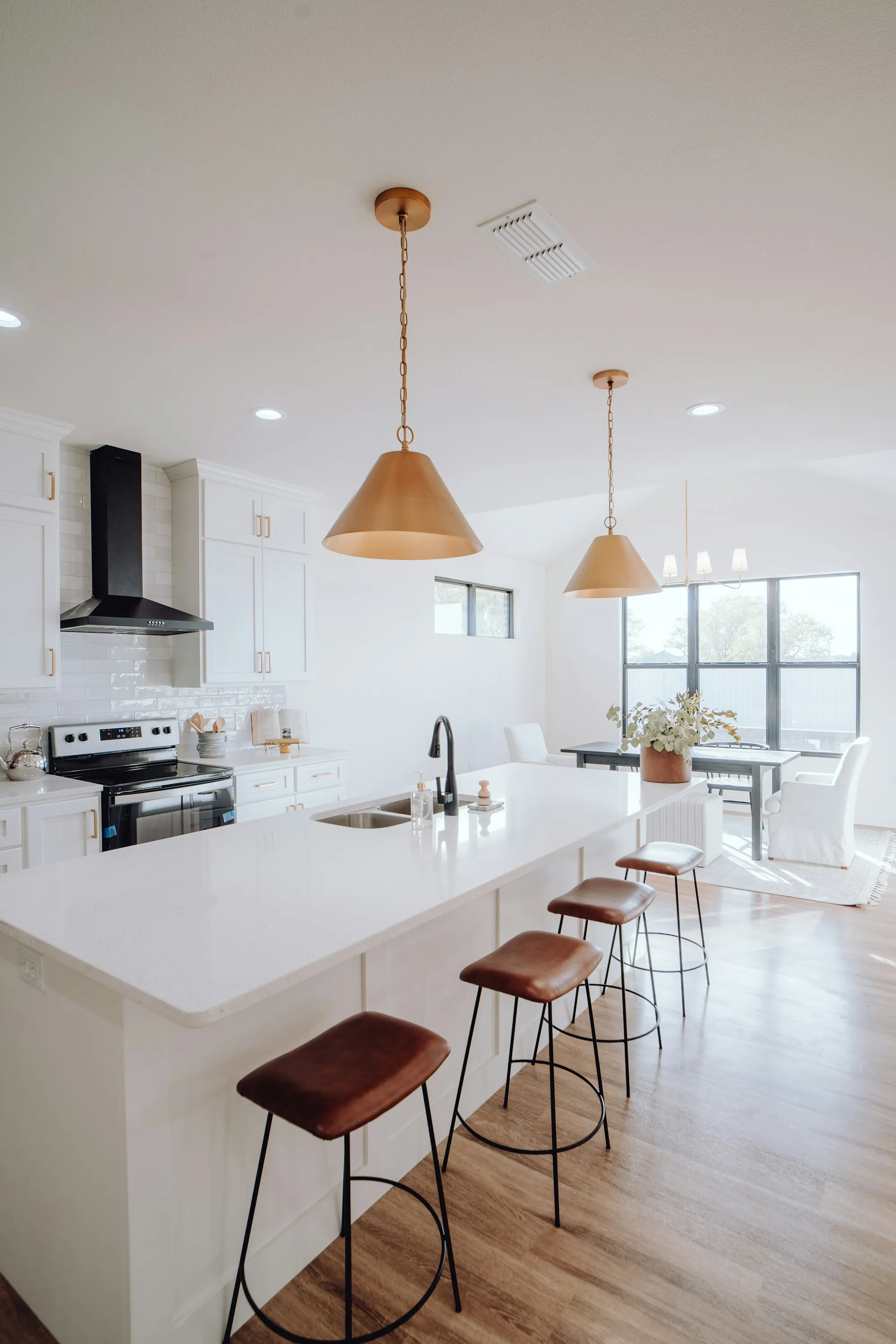 Bright kitchen with a white island, leather stools and copper pendant lights